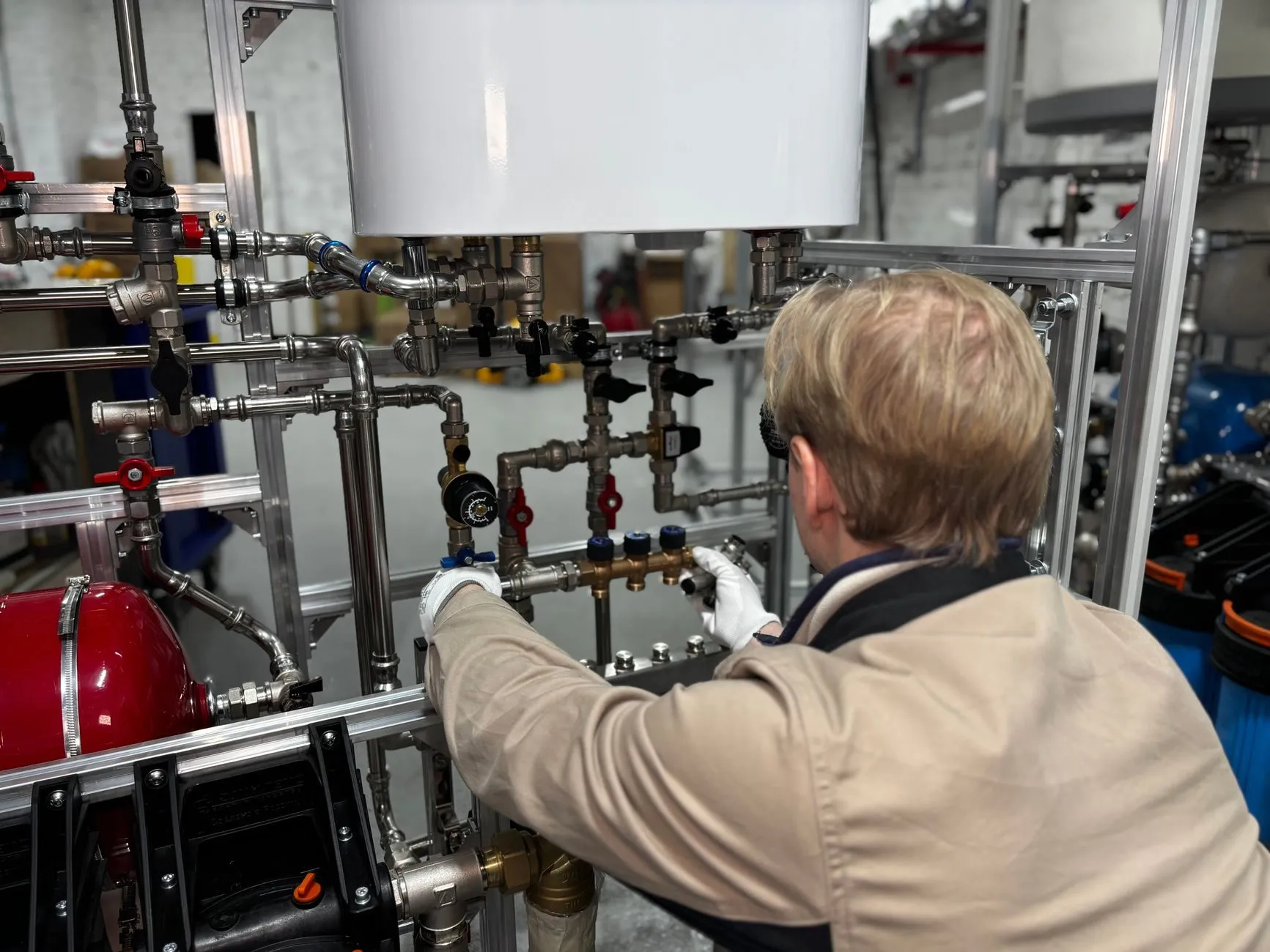 An engineer seen from behind, adjusting valves on a heating pipework rig in the workshop