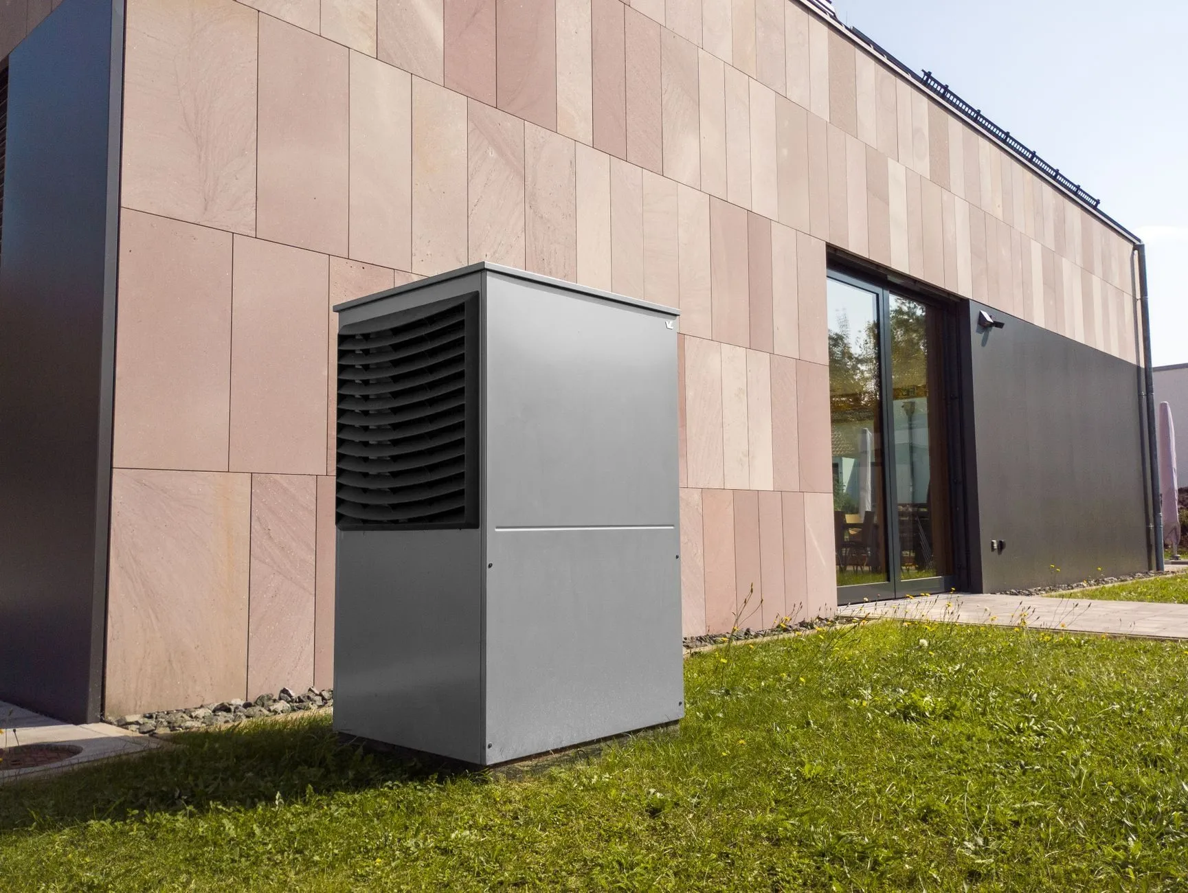 A floor-standing heat pump on a lawn beside a modern house