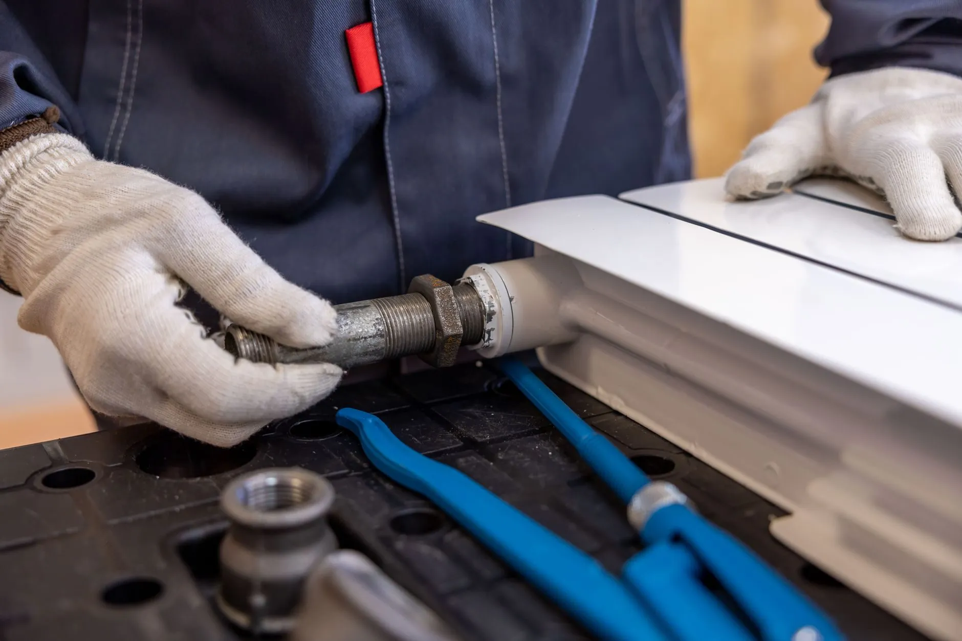 Gloved hands fitting a threaded pipe connector to a new white radiator