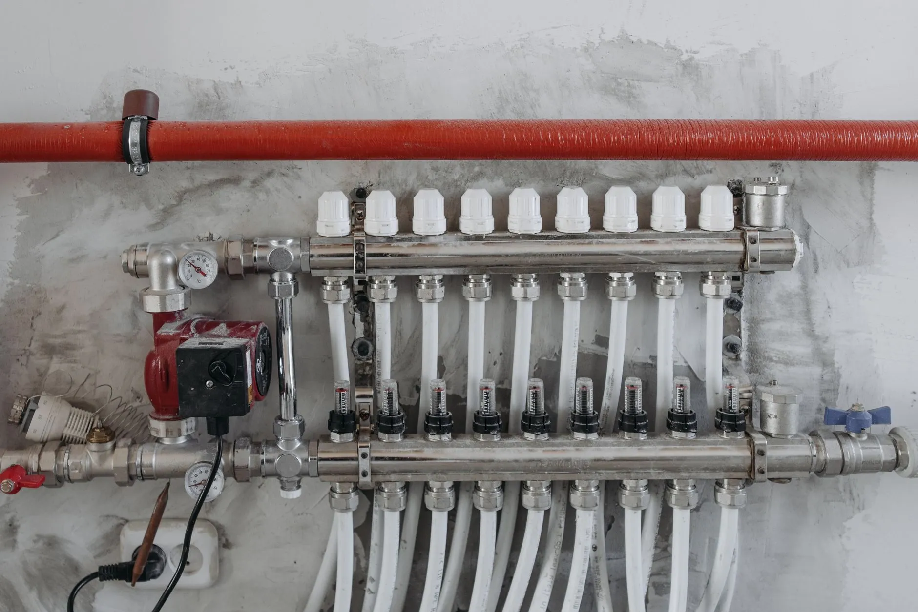 An underfloor heating manifold with a circulating pump and pressure gauge on a plastered wall